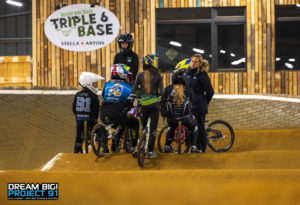 BMX-coach begeleidt een kind tijdens een veilige techniektraining op het BMX-parcours.